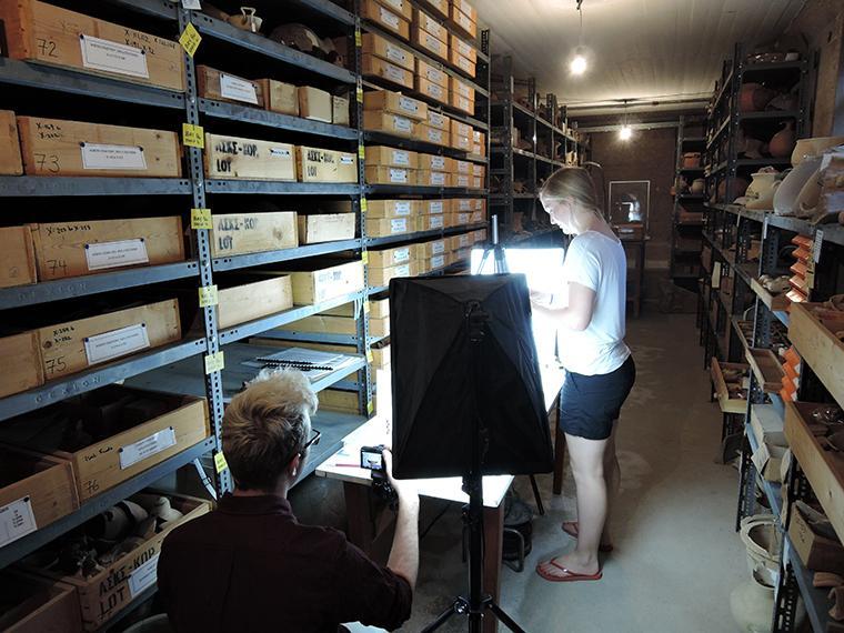 People working in an archive or storage room with shelves filled with boxes.