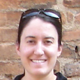 A person smiling in front of a brick wall.