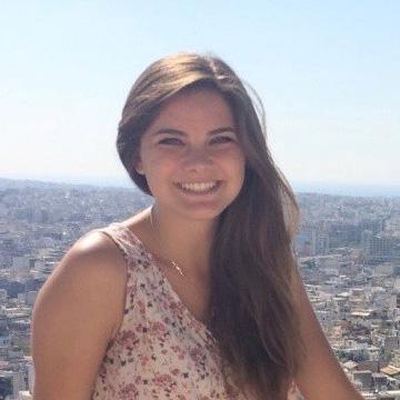 A woman smiling outdoors with a cityscape in the background.
