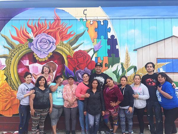 Madres, and mural making support team, from Guadalupe Washington posing before their community mural, Madres Emprendedoras: Mosaicos de la Comunidad.