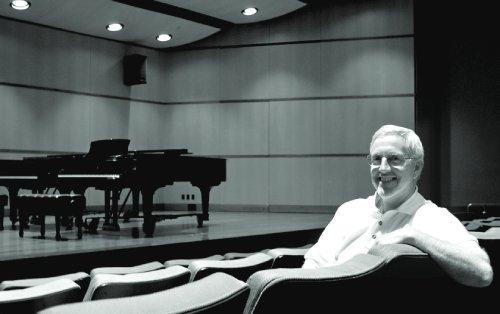 Butch Coyne in theatre seats in front of a stage with a piano