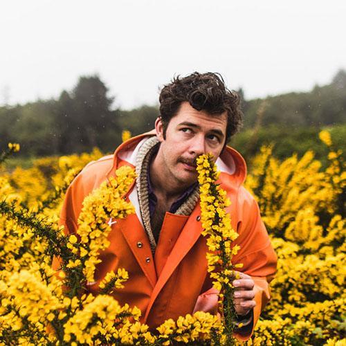 Neil Ferron wearing an orange rain coat in a field of yellow flowers