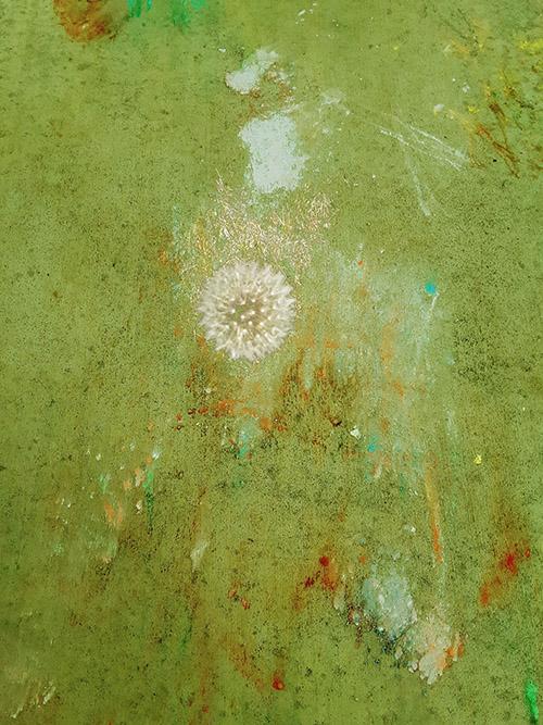 An art piece that has a variously shaded green background with an out of focus dandelion
