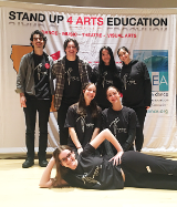 Seven SCU dancers, theatre artists and musicians pose in front of a sign saying Stand Up 4 Arts Education in Sacramento.