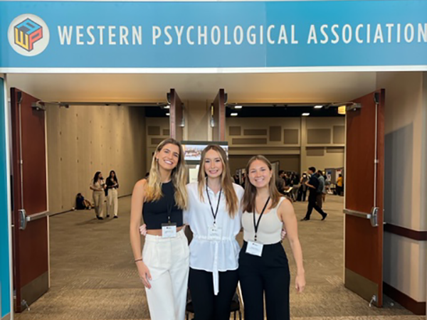 Isabella Meyerhoff, Grace Roach, and Hayley Harrison standing in front of the entranace to the104th annual Western Psychological Association conference