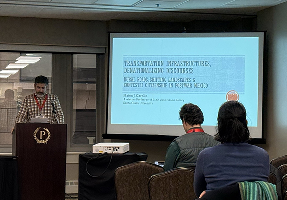 Mateo Carillo standing at a podium in from of a screen presenting at a conference