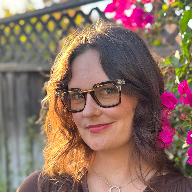 Leah Senatro headshot - outdoors next to a fence and flowery bush