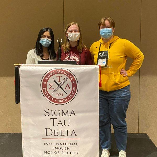 Three students at a podium that says Sigma Tau Delta International English Honor Society