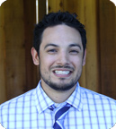 A person smiling, wearing a checkered shirt with a tie. image link to story