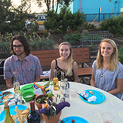 Three people sitting at a table outdoors with food and drinks.