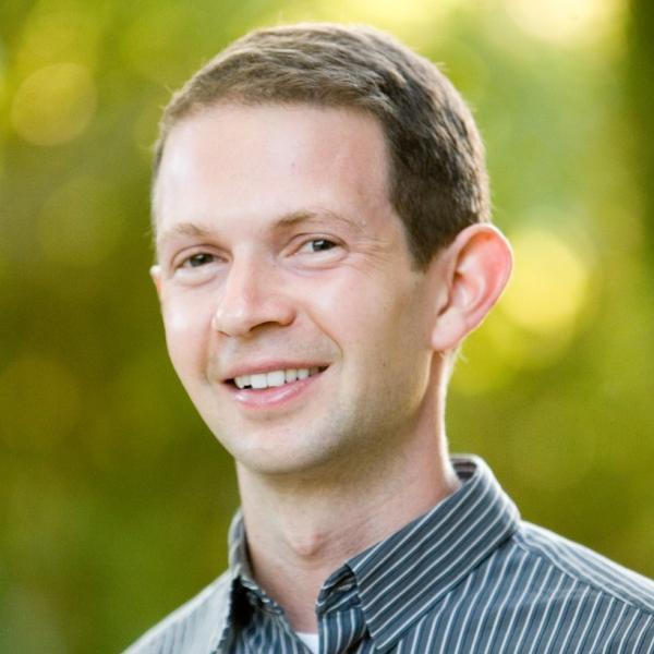 A person smiling outdoors with a blurred green background. image link to story