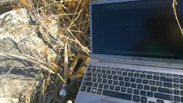 Open laptop next to a moss-covered rock outdoors.