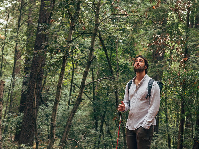 A young man with long hair and a beard wearing a button up shirt, walking through the words.