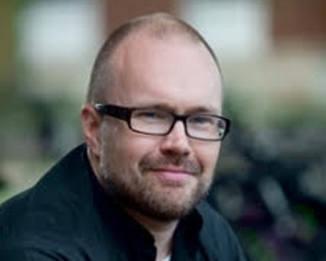 A person with glasses smiling outdoors.