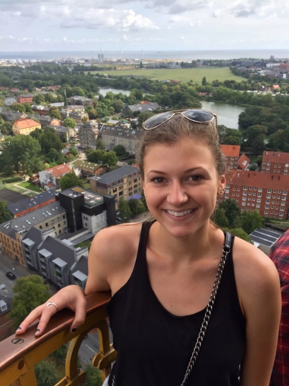 Woman smiling with a scenic view of a town behind her. image link to story