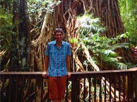 A person posing in front of a large tree within a lush forest. image link to story