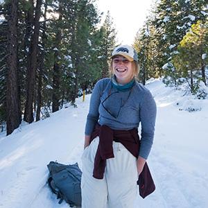 A person smiling on a snowy trail with trees in the background.
