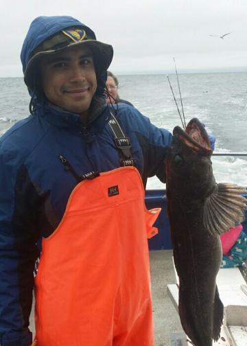 Person holding a fish on a boat while wearing orange and blue clothing.