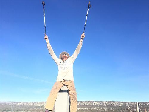 Person celebrating on a mountaintop with arms raised under a clear blue sky. image link to story