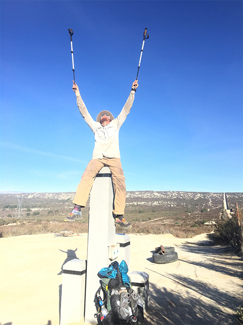 Person celebrating on a mountaintop with arms raised under a clear blue sky.