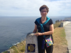 Person standing beside a marker near the coast with the sea and sidewalk. image link to story
