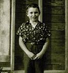 A young person standing in front of a wooden wall wearing a patterned shirt.