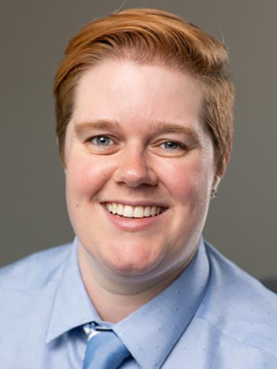 A smiling person in a blue shirt and tie.