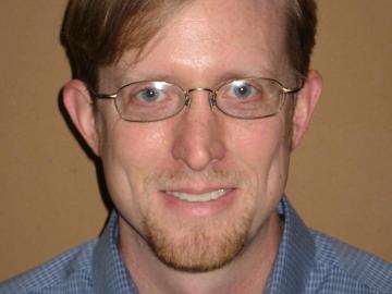 Person wearing glasses and a blue shirt against a brown background.