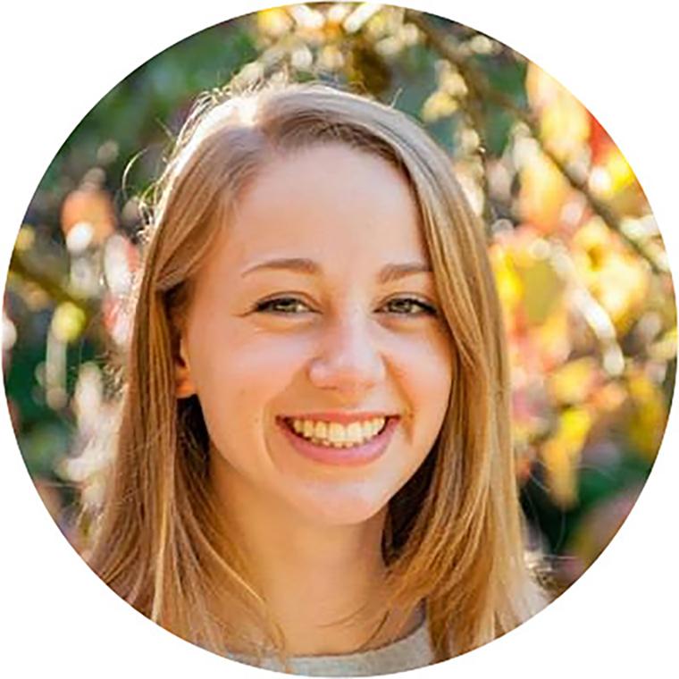 Smiling person outdoors with blurred foliage background.