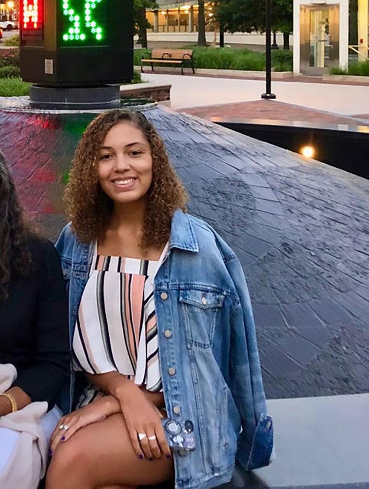 A person dressed casually sitting outside near a reflective pool.