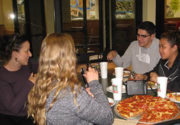 People sharing pizza and drinks around a tablear at a casual gathering.