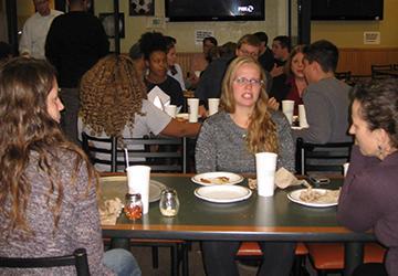 People sitting around tables, eating pizza, and talking.