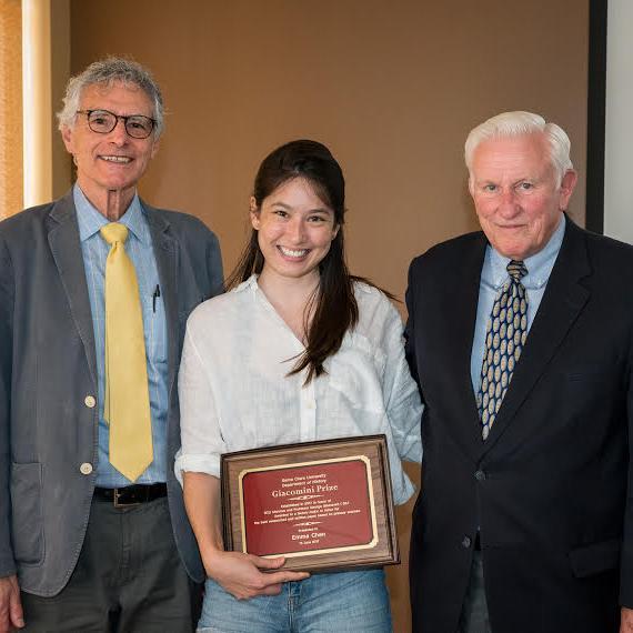Three people standing; person in the middle holds a framed plaque.