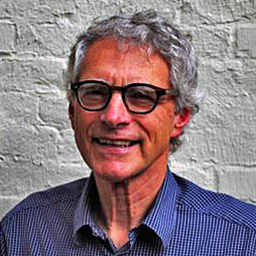 A man with glasses against a brick wall background.