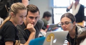 Three people working together on a laptop in a classroom setting. image link to story