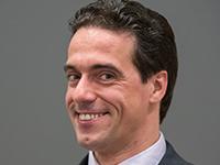 Smiling person in a suit against a gray background.