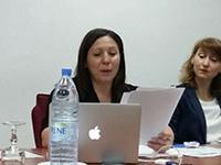 Two women at a table, one speaking, with a laptop and papers.