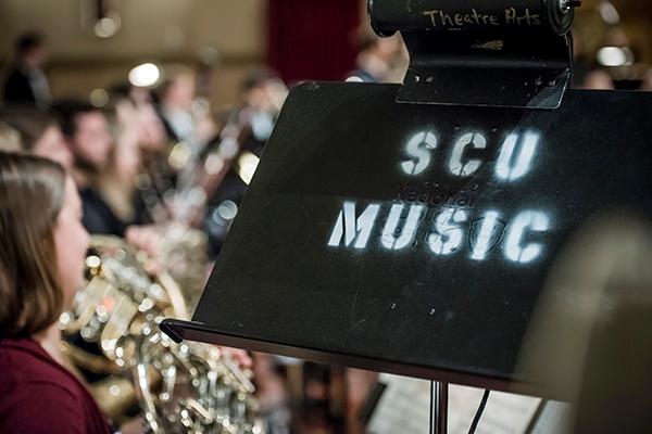 Zoom in of a music stand with SCU Music on it with students playing in the background