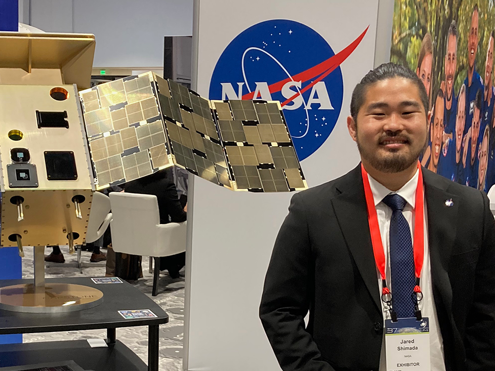 Jared Shimada standing next to NASA logo and display
