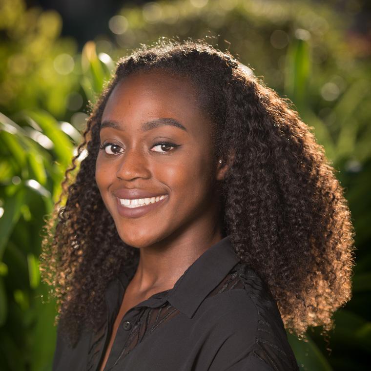 A woman smiling with greenery in the background.