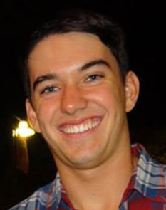 A smiling person wearing a plaid shirt at night.