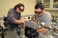 Two people working with scientific equipment, wearing protective eyewear in a laboratory setting.