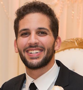 A person smiling, wearing a suit with a white boutonnière image link to story