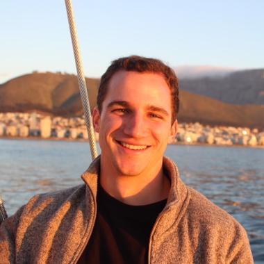 A person smiling in front of a scenic waterfront view. image link to story