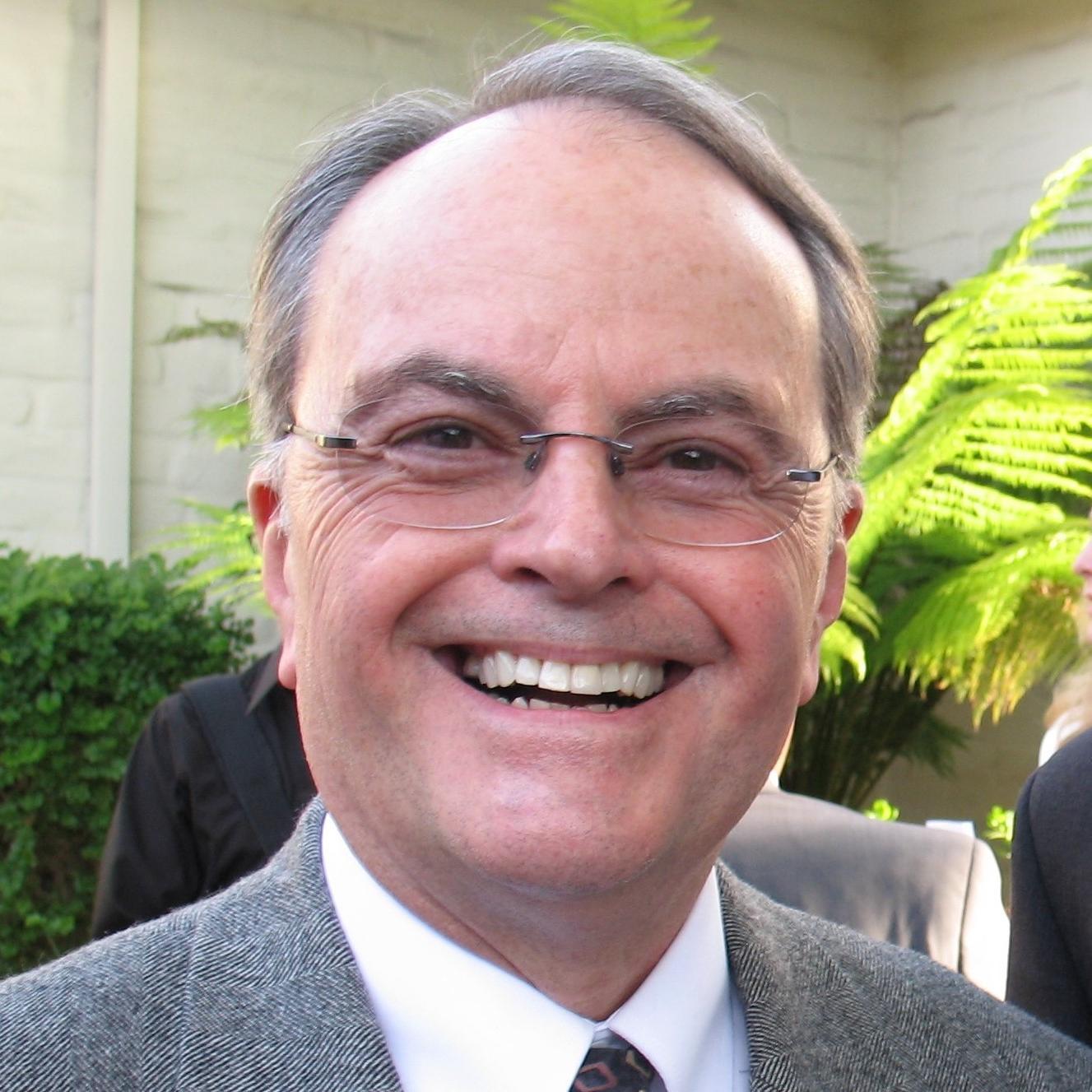 A man in a suit and tie smiling outdoors. image link to story