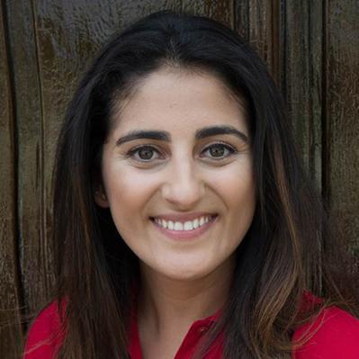 A person in a red shirt smiling in front of a wooden background. image link to story