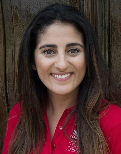 A person in a red shirt smiling in front of a wooden background. image link to story