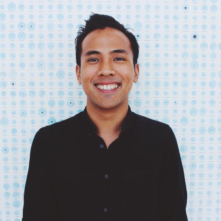 A person smiling in front of a tiled wall background.
