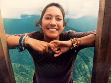 A person smiling and leaning on a wooden railing, with a mountainous background. image link to story