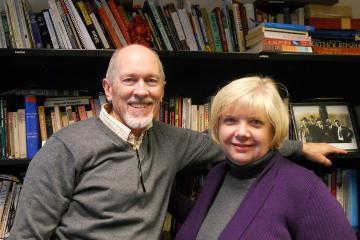 Two people smiling in a library, shelves of books in the background. image link to story